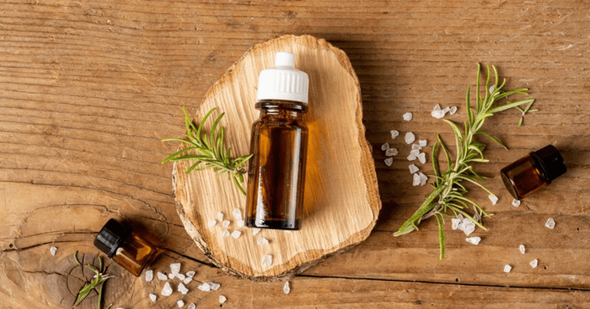 A bottle of Rosemary Essential Oil for Hair Growth placed on a wooden surface with fresh rosemary sprigs.